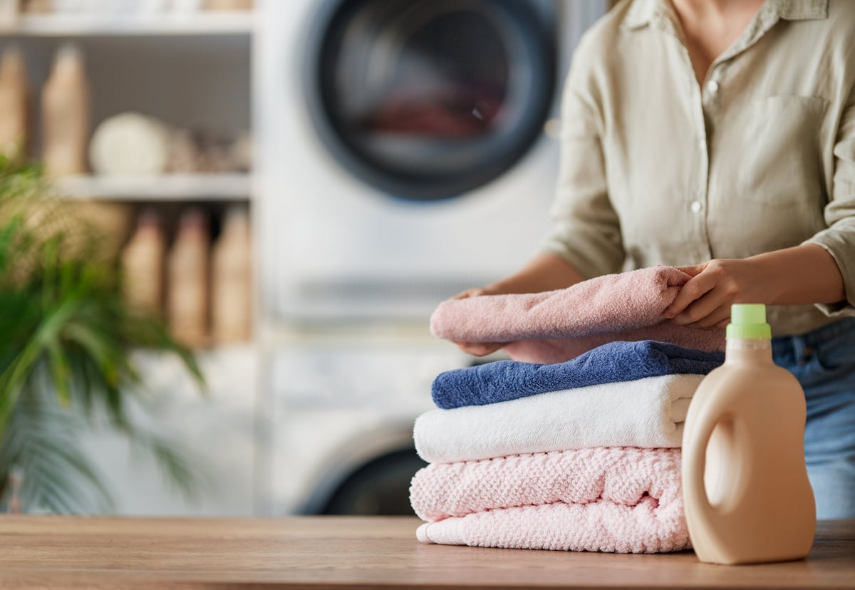 A woman peacefully folding fresh, clean towels beside a washing machine